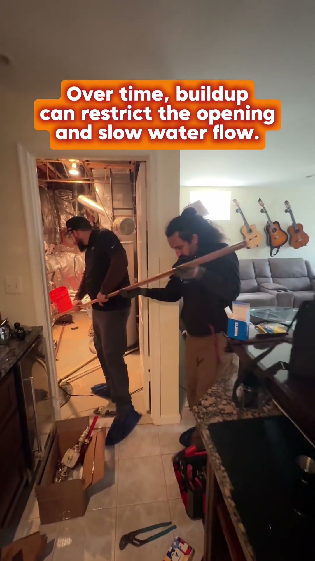 Plumbing job in a home: a gloved hand tags a brass valve assembly near a red bucket, two techs carry a long copper pipe through a kitchen to a utility closet, and a tech kneels to fit pipe in the clos